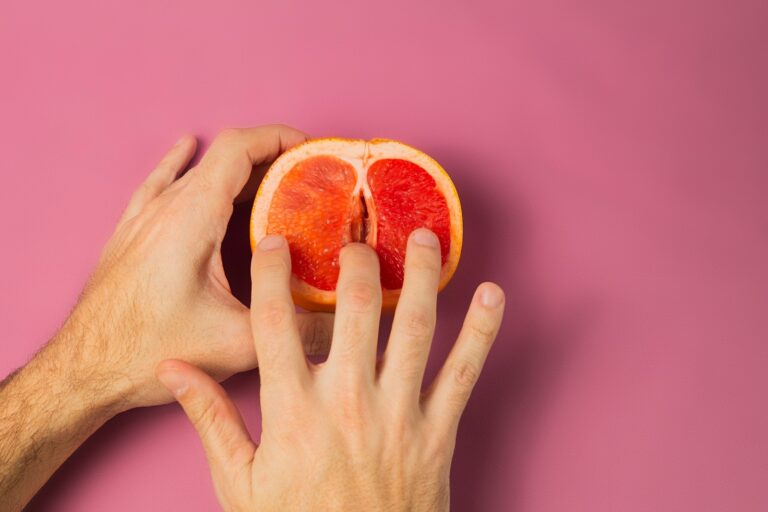 Overhead of crop unrecognizable person sticking finger into half of fresh grapefruit against pink background