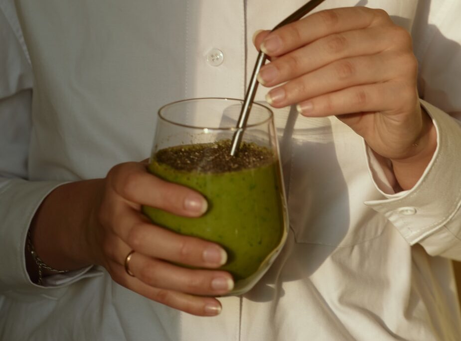 person in white button up shirt holding clear drinking glass with green liquid